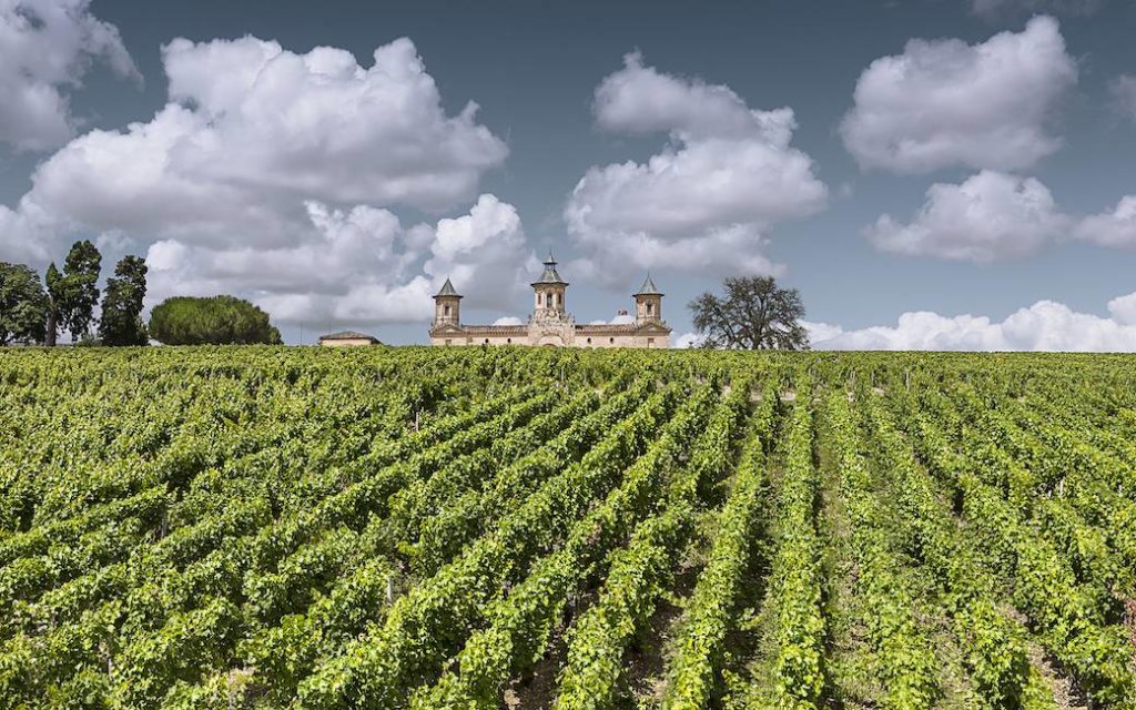 Château Cos d'Estournel, a grand estate in the Medoc region, surrounded by expansive vineyards under a cloudy sky, showcasing its iconic architecture and lush grapevines.