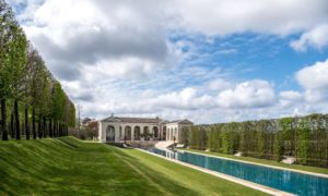 Elegant château with manicured gardens and a long reflective pool in Bordeaux, showcasing luxury and tranquility during a Medoc wine tour.