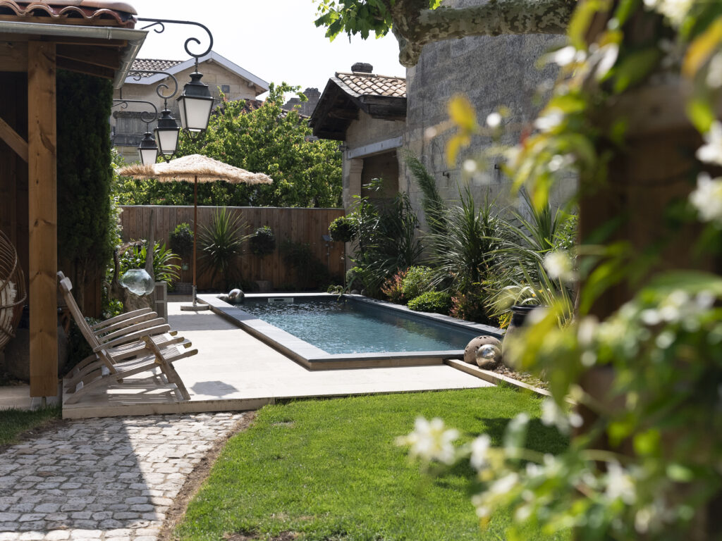 A serene garden pool surrounded by lush greenery and cozy seating at a Bordeaux villa, offering luxurious accommodation for wine tour guests.