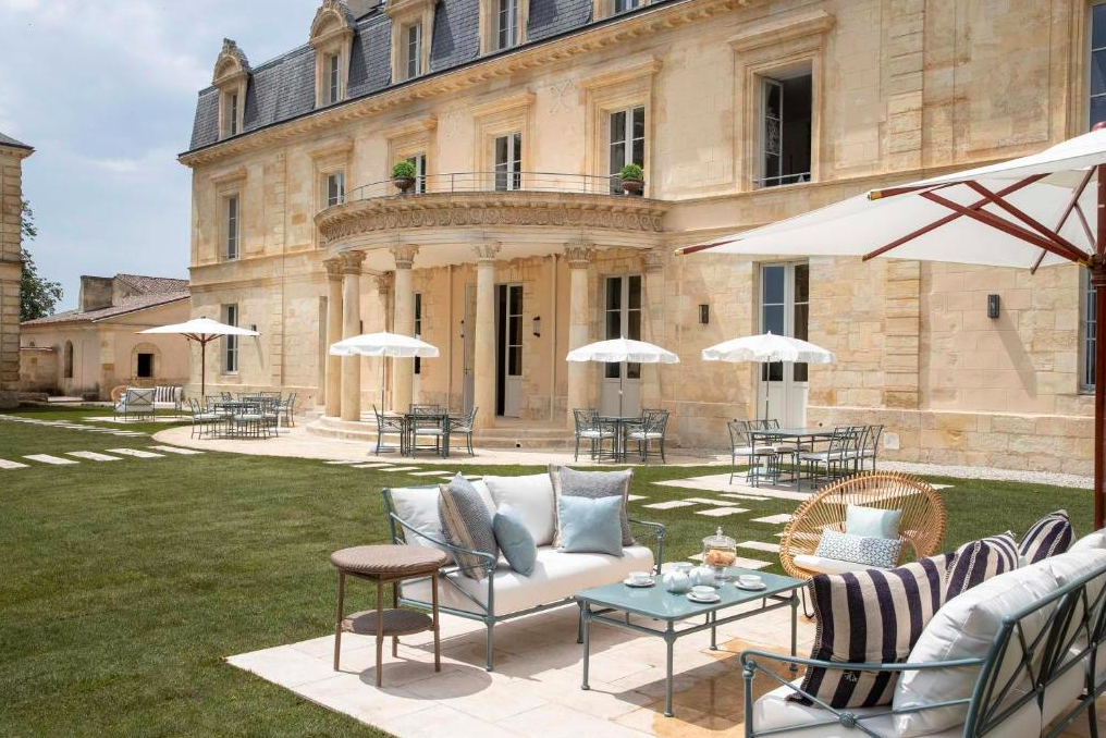 Luxurious outdoor seating area at Maison d'Estournel, featuring elegant furniture and umbrellas, set against the backdrop of a historic Bordeaux estate during a Medoc wine tour.